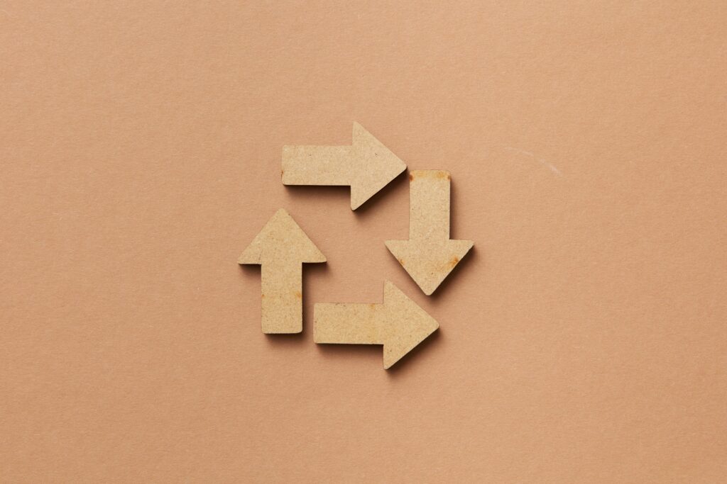 pexels photo 7679935 7679935 Close-up of a recycling symbol made from wooden arrows on a beige background.